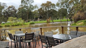 A wooden deck with outdoor seating and a view of a pond surrounded by trees. - Magdala Motor Lodge & Lakeside Restaurant (Stawell)