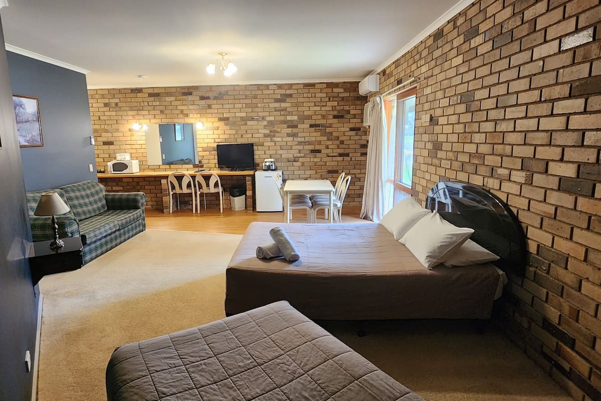 A cozy room with a brick wall, a bed, a sofa, a desk with a chair, and a TV.