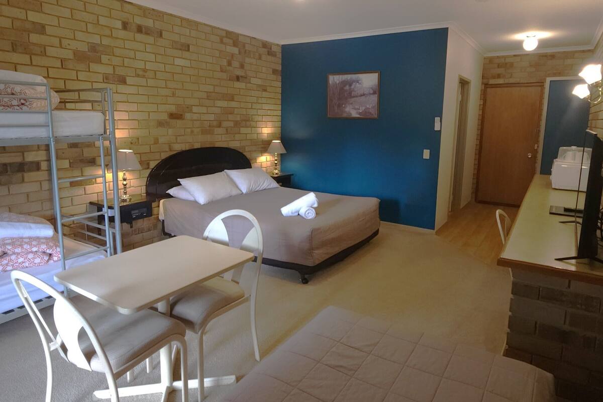 A room with a bunk bed, a desk with a chair, a small table, and a lamp.