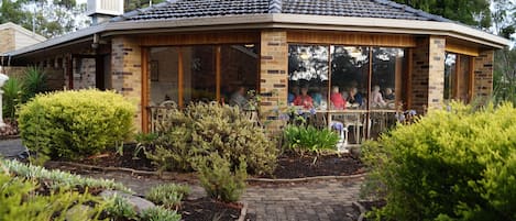 A gazebo with a tiled roof and brick walls, surrounded by landscaped gardens and a brick pathway.