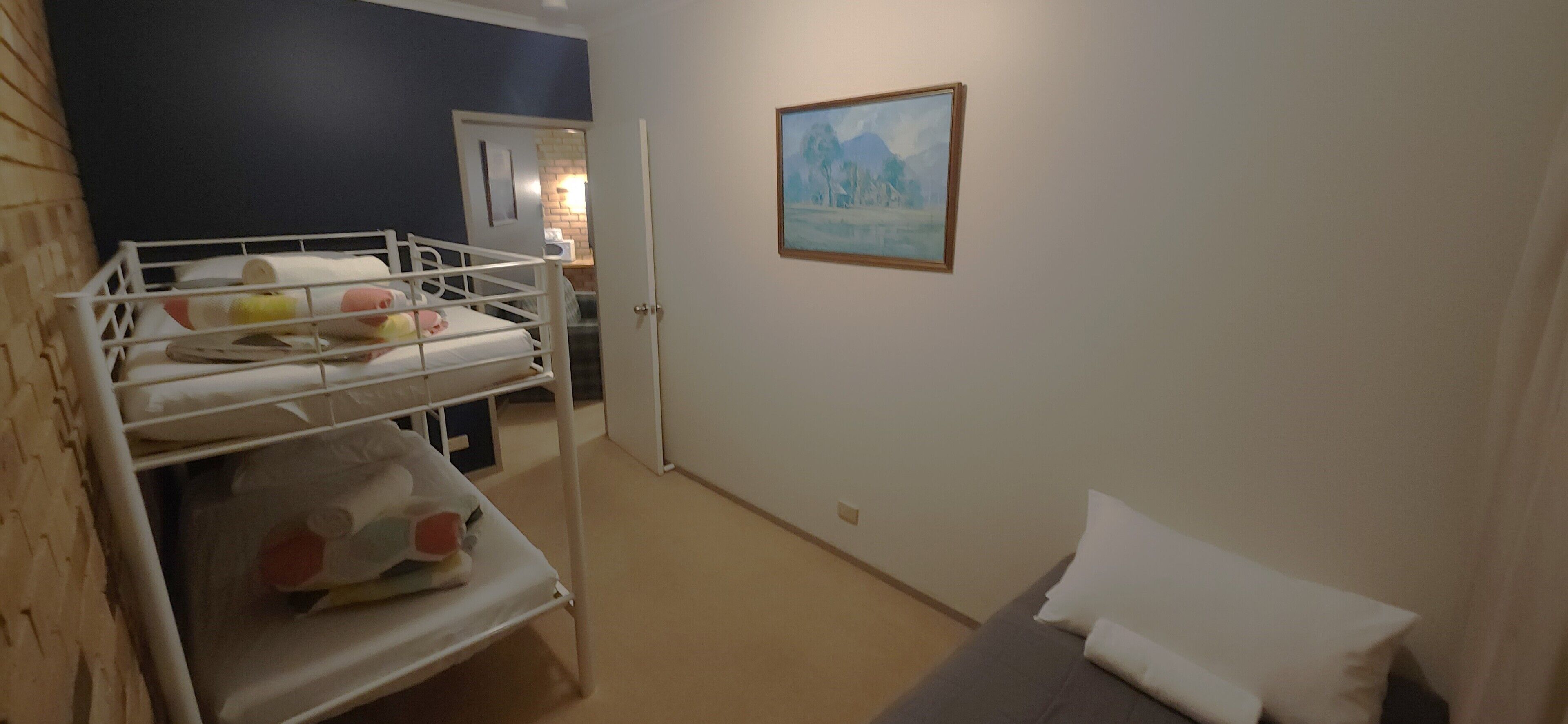 Una habitación con literas, un sofá gris, un cuadro en la pared y una puerta que da a otra estancia.