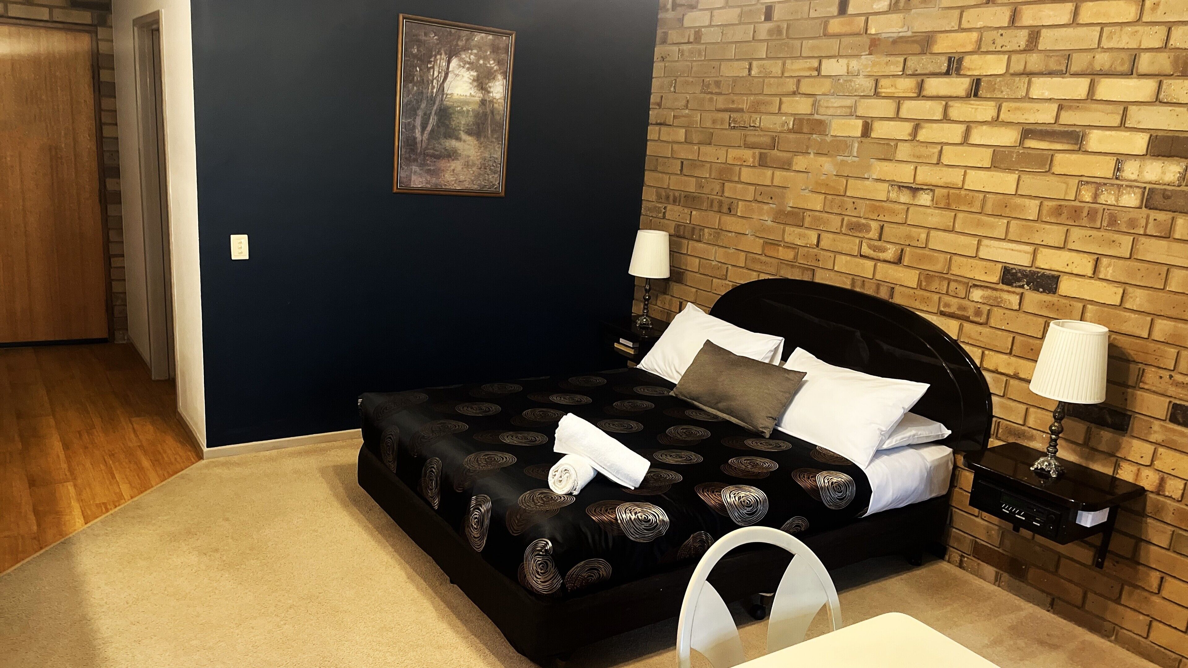 A bedroom with a black bed, white pillows, and a painting on the wall.