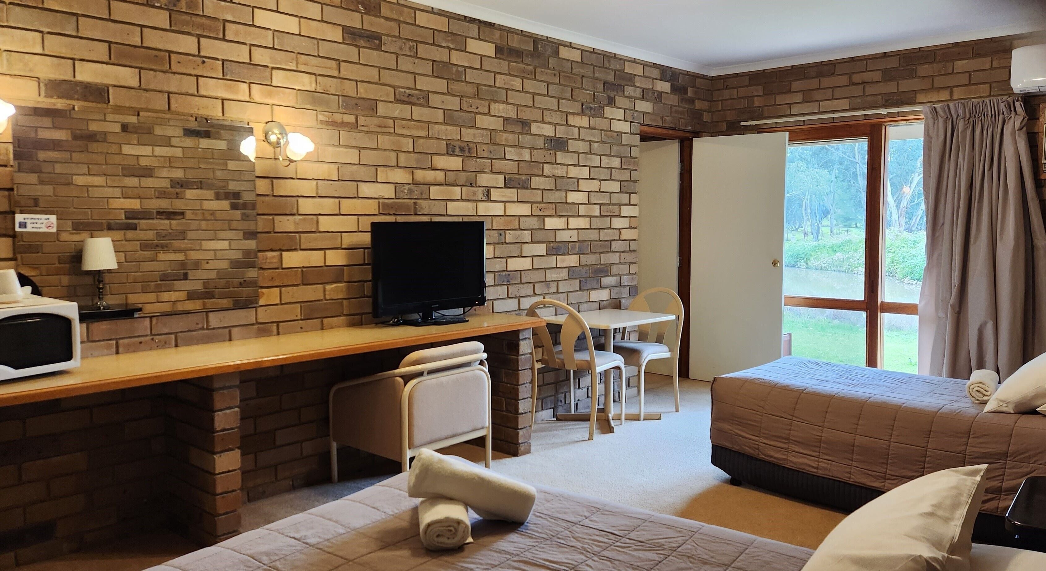 Habitación de hotel con pared de ladrillo, un escritorio con computadora, cama y vista al exterior.