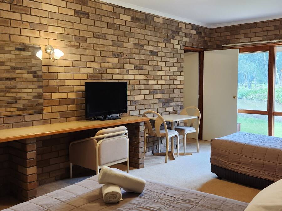 Ein Hotelzimmer mit Backsteinwand, einem Schreibtisch mit Computer, einem Bett und Blick ins Freie.