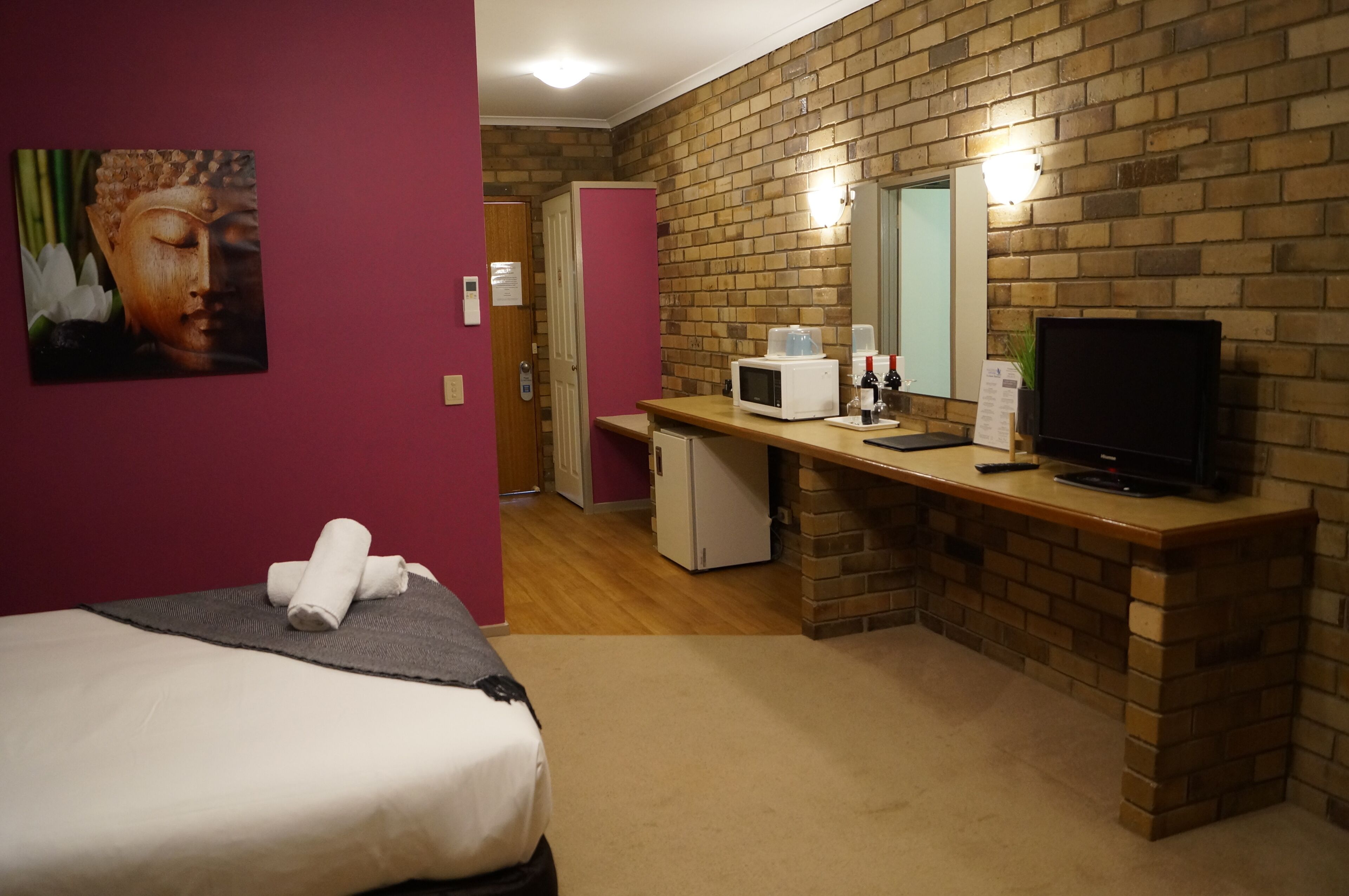 Ein Hotelzimmer mit Bett, Schreibtisch, Mikrowelle, Fernseher und einer Ziegelwand.