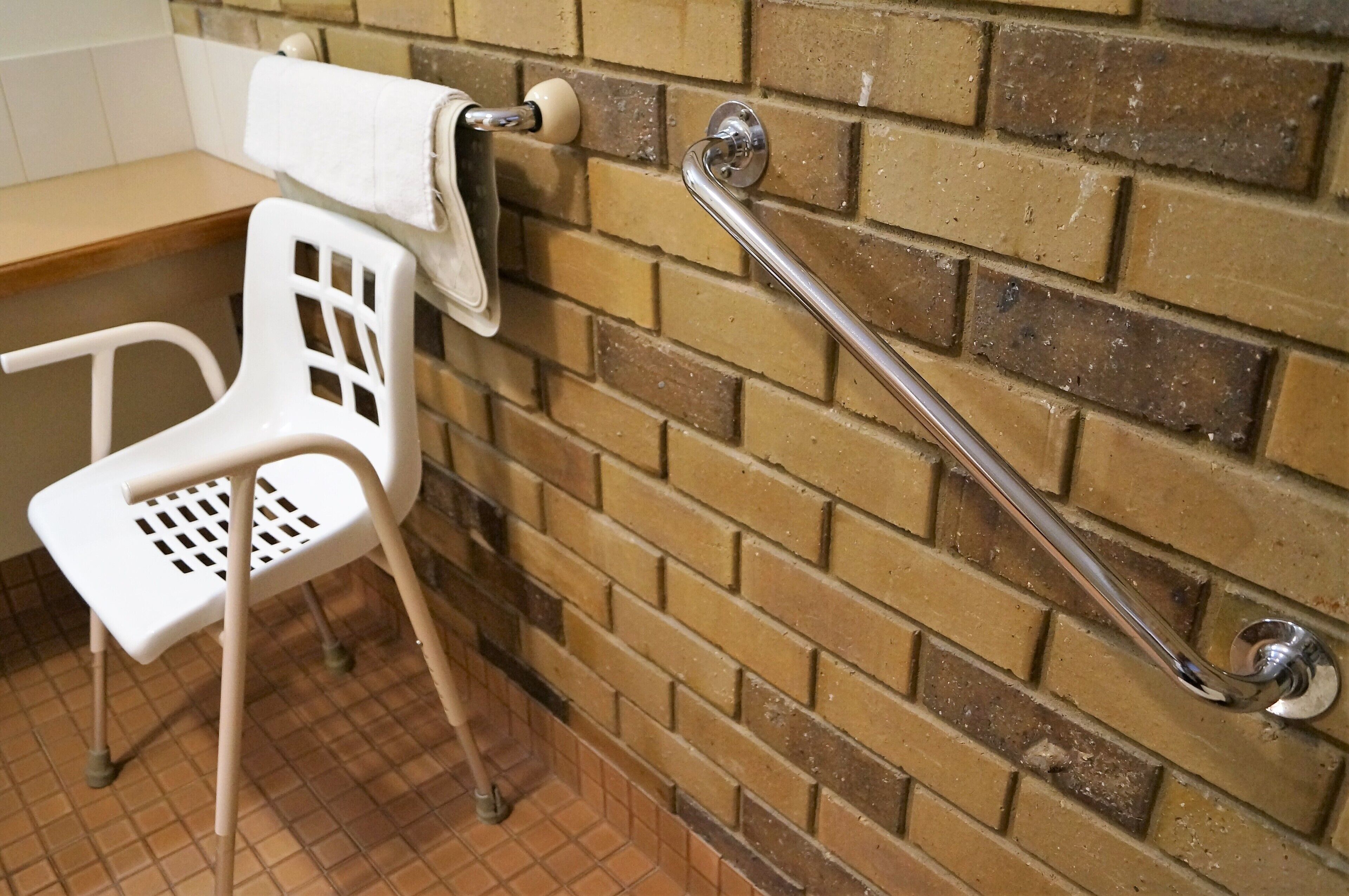 A bathroom with a white plastic chair, a towel rack, and a grab bar.