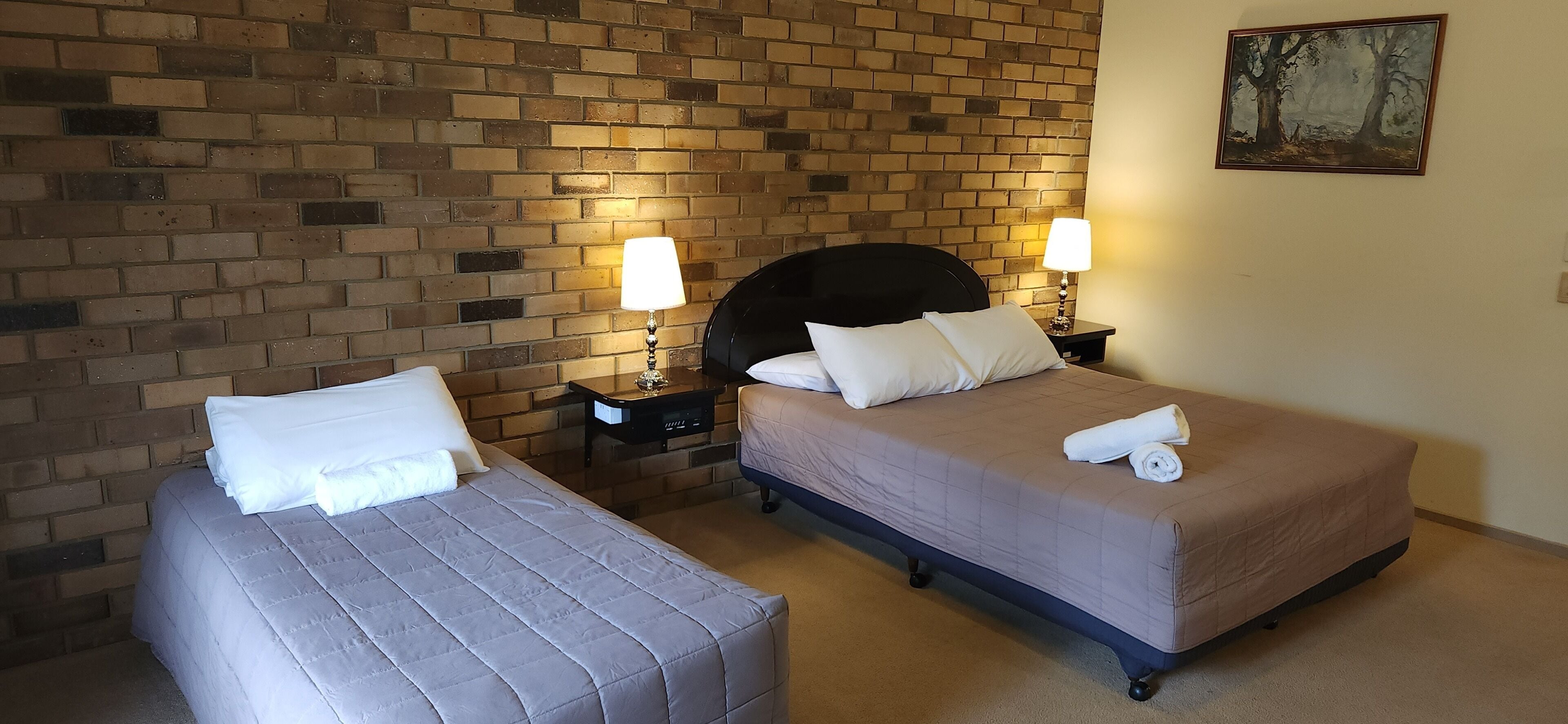 A hotel room with two beds, a brick wall, and a painting.
