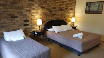 A hotel room with two beds, a brick wall, and a painting.