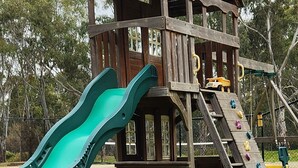 A wooden playhouse with a green slide and climbing wall. - Magdala Motor Lodge & Lakeside Restaurant (Stawell)