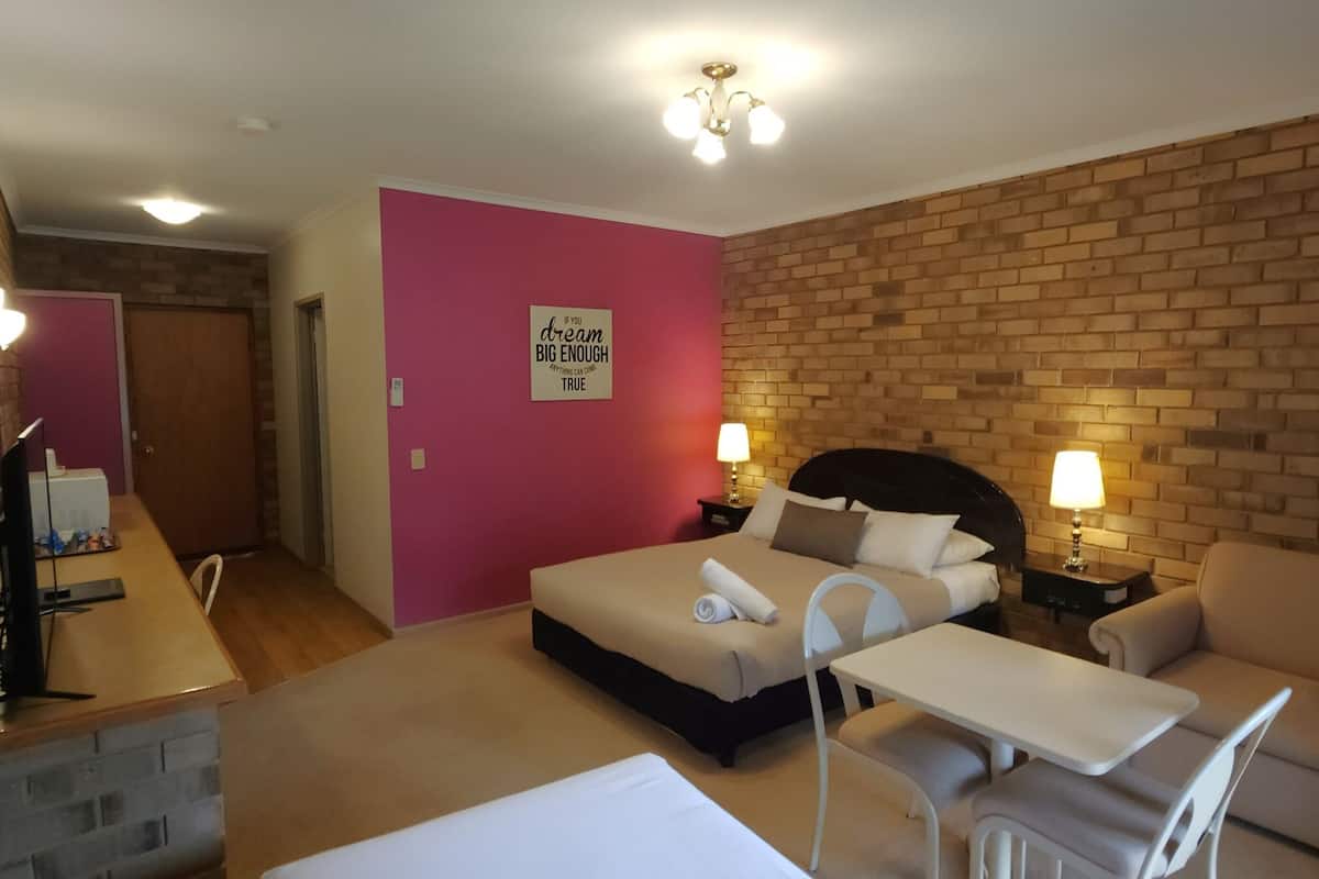 A hotel room with a bed, a small table, a sofa, and a brick wall.