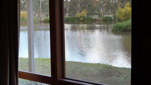 A view through a window of a calm lake with surrounding greenery. - Magdala Motor Lodge & Lakeside Restaurant (Stawell)