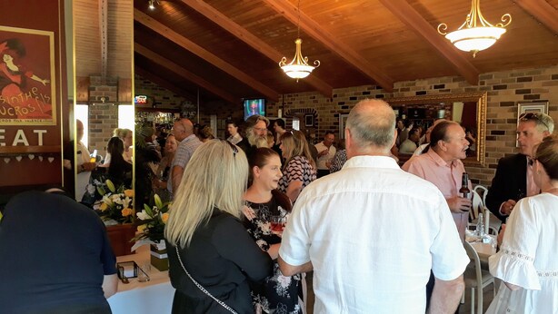 A crowded indoor venue with wooden beams and brick walls, featuring a chandelier and a television screen. - Magdala Motor Lodge & Lakeside Restaurant (Stawell)