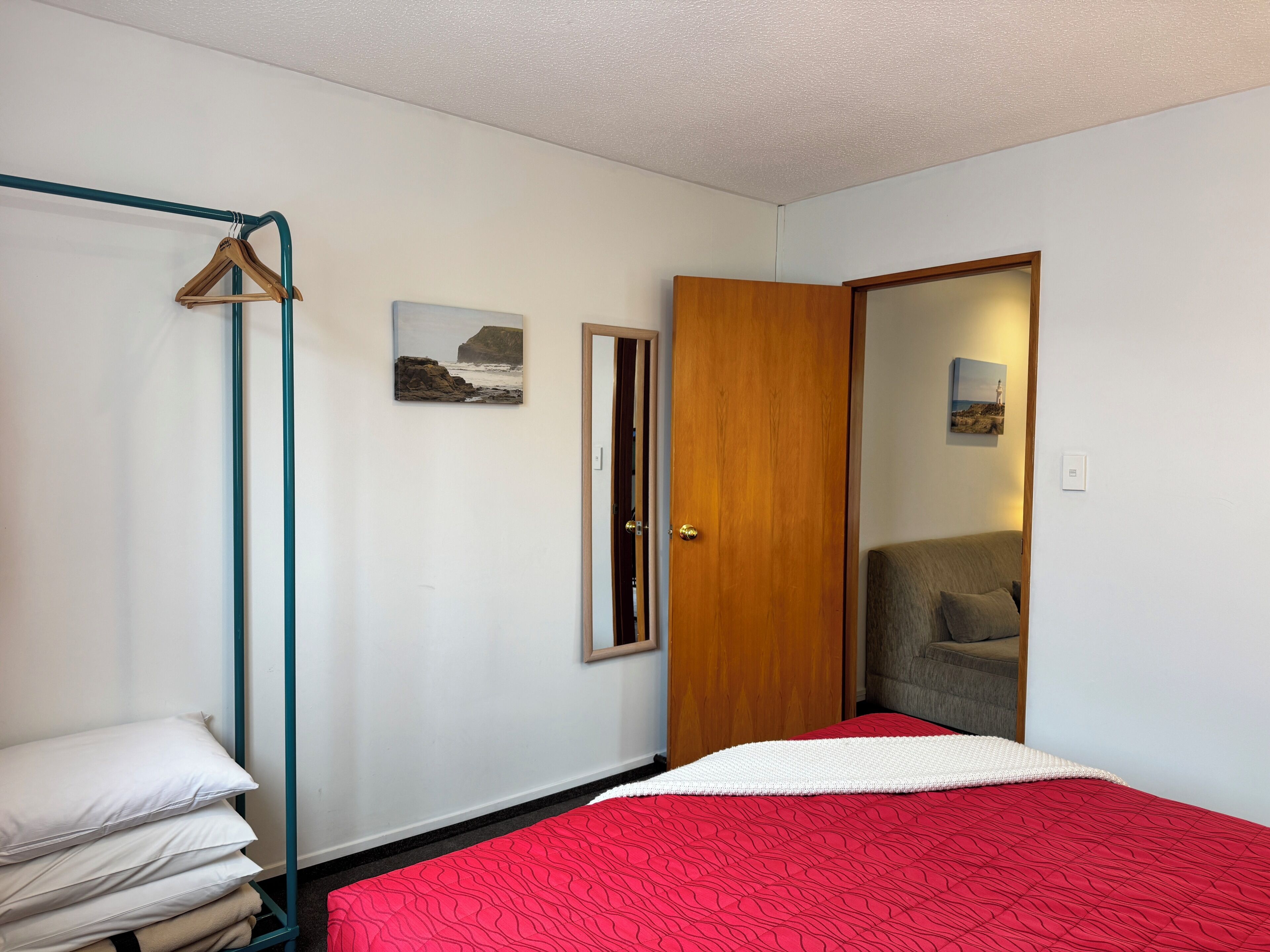 A bedroom with a bed, a wooden door, a coat rack, and a wall-mounted picture.