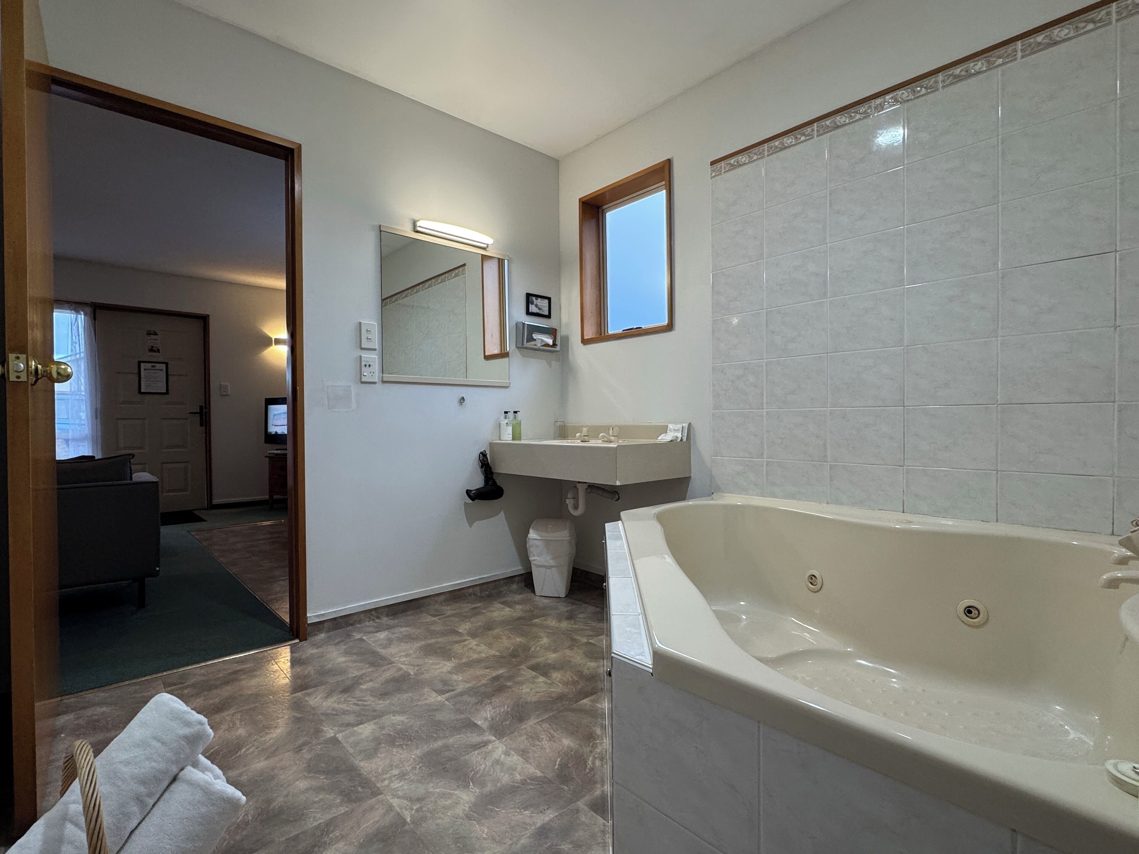 A modern bathroom with a large bathtub, a vanity with a mirror, and a small window.