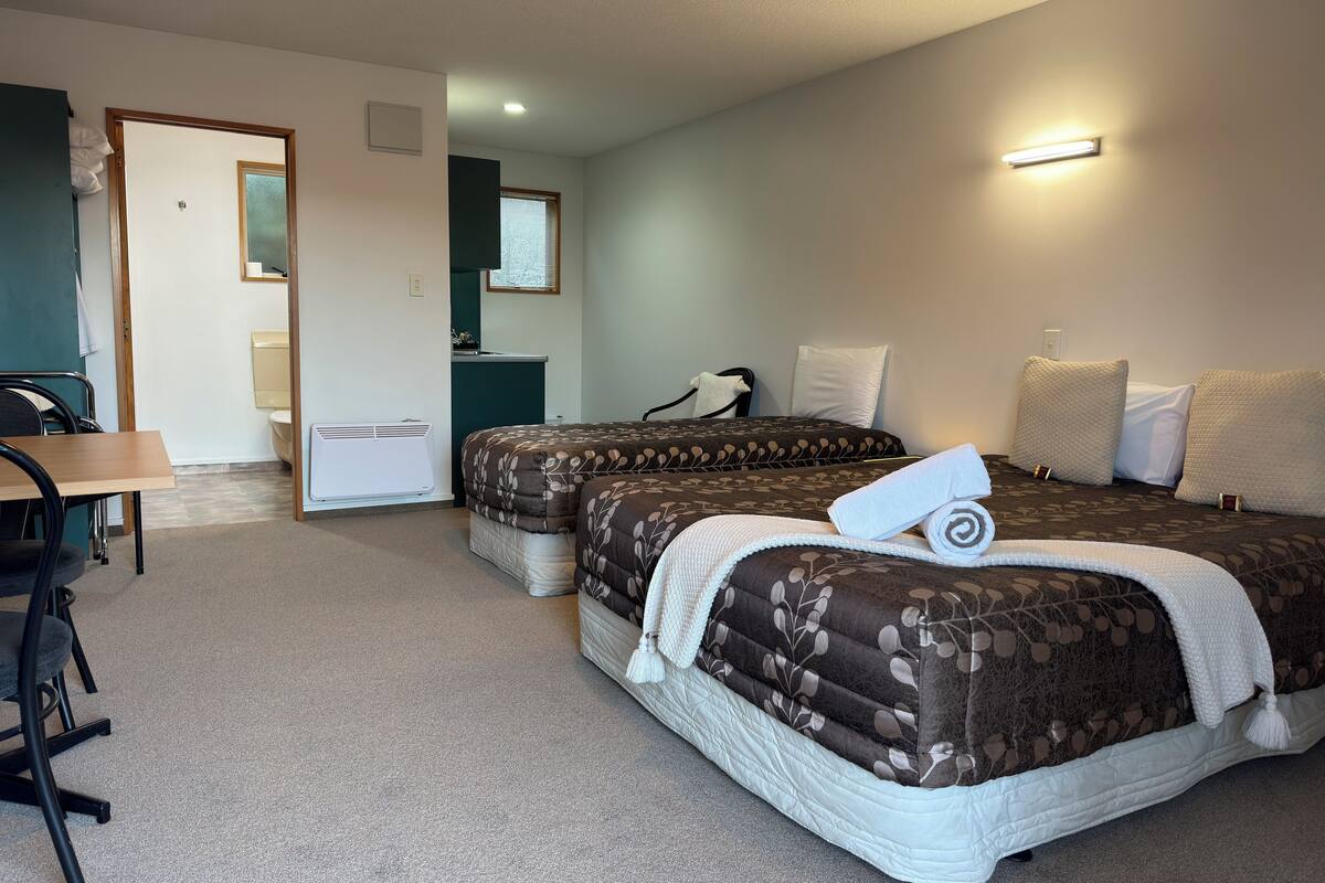 A hotel room with two beds, a desk, a chair, a small kitchenette, and a bathroom.