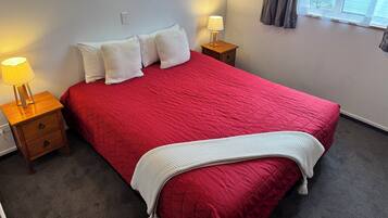 A neatly made bed with a red bedspread, two white pillows, a white throw blanket, and two bedside lamps on wooden nightstands.
