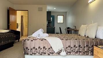A bedroom with a large bed, a desk, and a chair. There is a door leading to another room.