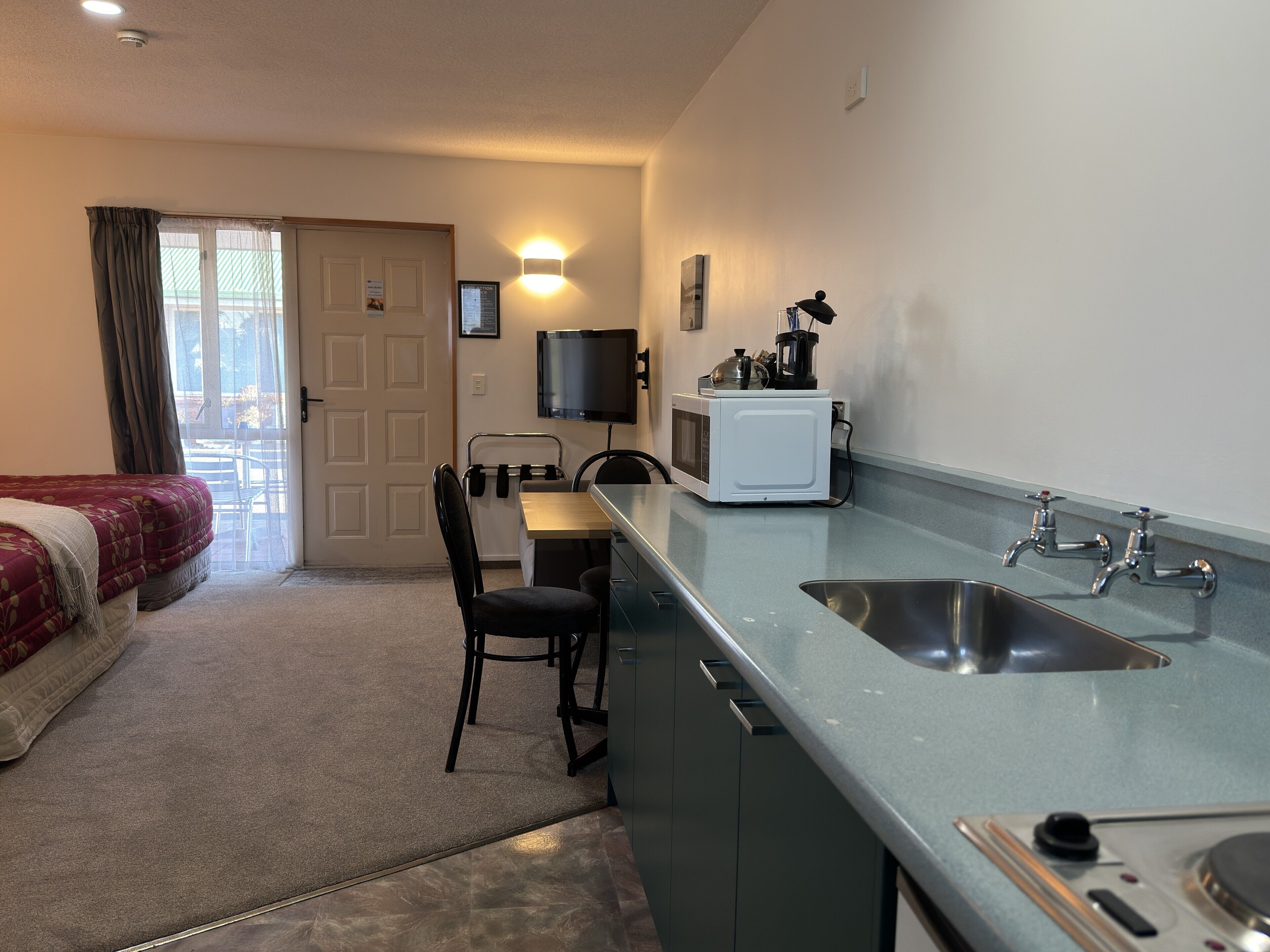 A compact hotel room with a bed, a kitchenette, a dining area, and a bathroom.