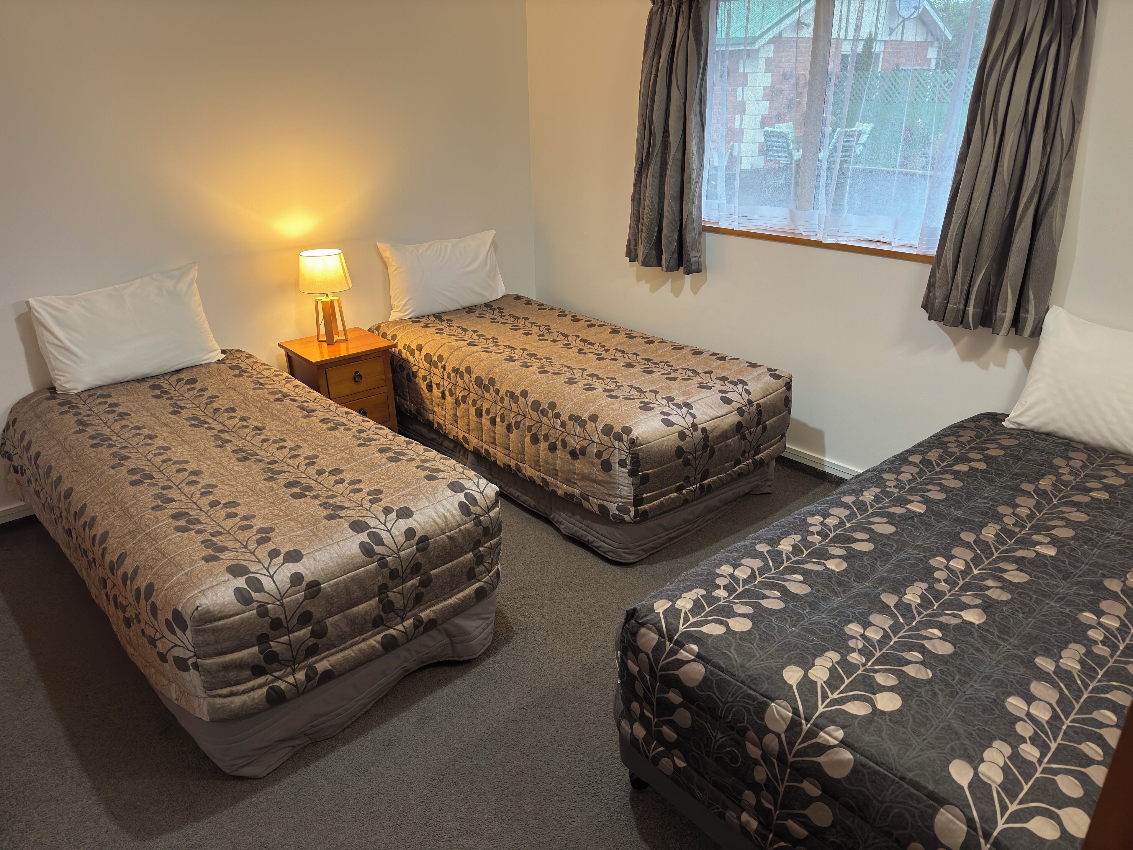 A room with two single beds, a nightstand with a lamp, and a window with curtains.