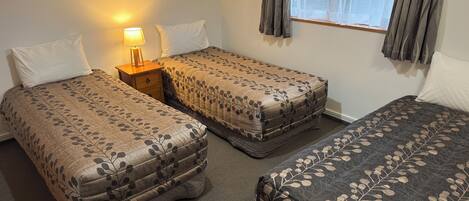 A room with two single beds, a nightstand with a lamp, and a window with curtains.