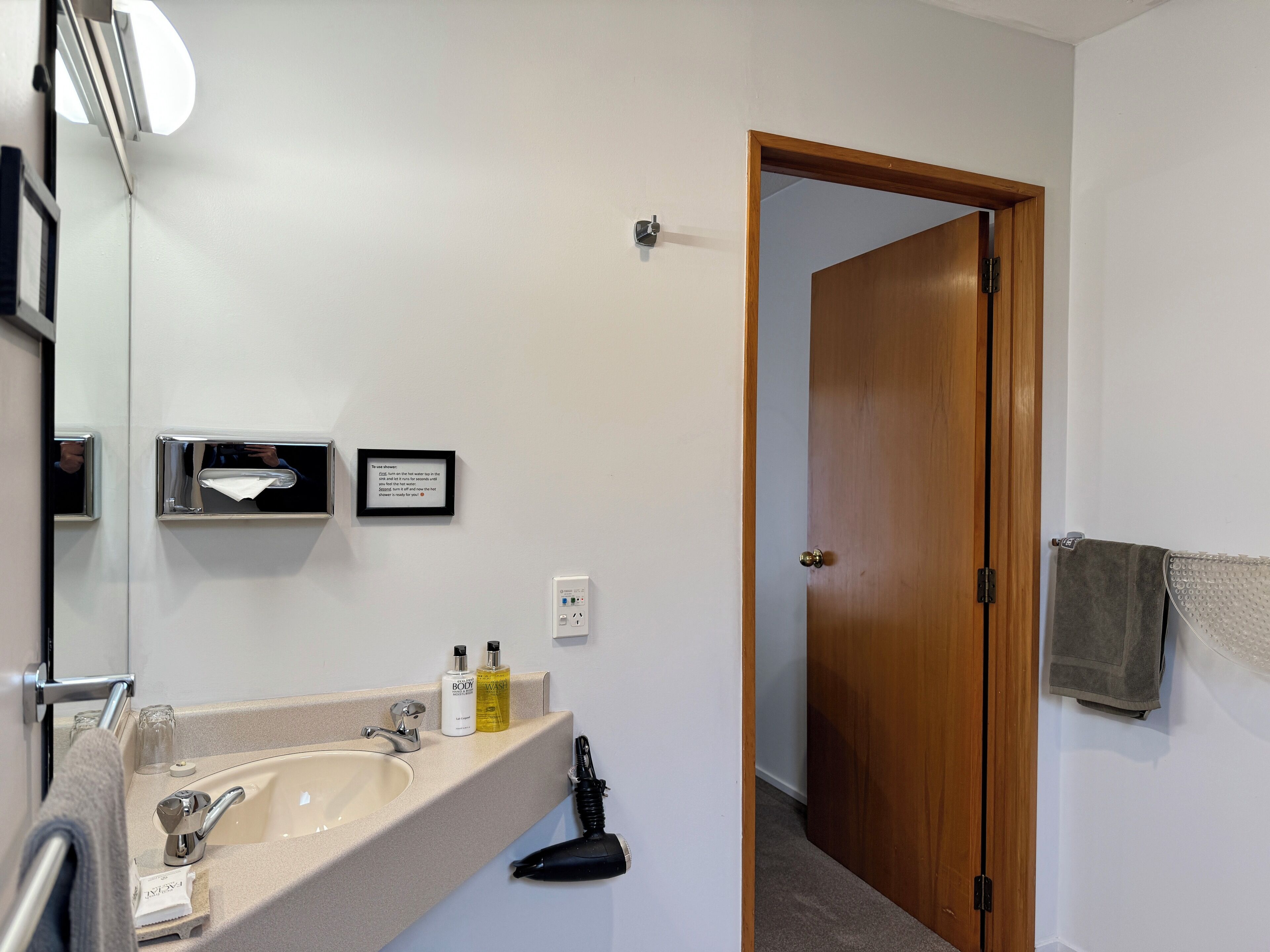 Une salle de bain équipée d’un lavabo, d’un miroir, d’un porte-serviettes et d’une porte donnant sur une autre pièce.