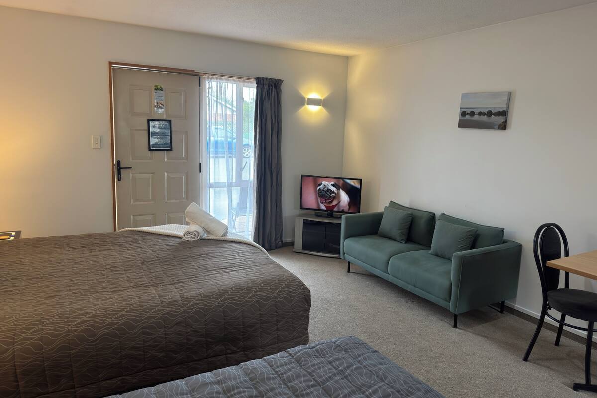 A hotel room with a bed, a green sofa, a TV, and a chair.