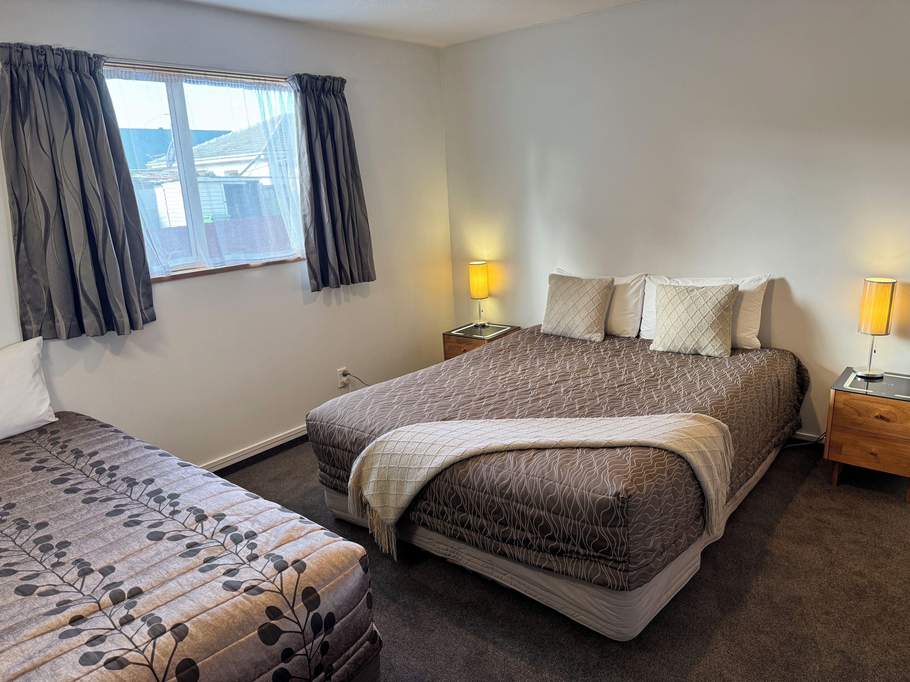 A bedroom with two beds, a window with curtains, bedside lamps, and a nightstand.