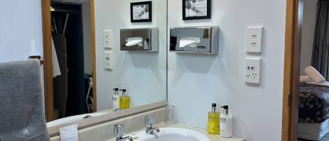 A hotel bathroom with a large sink, mirror, towel rack, and a trash bin.