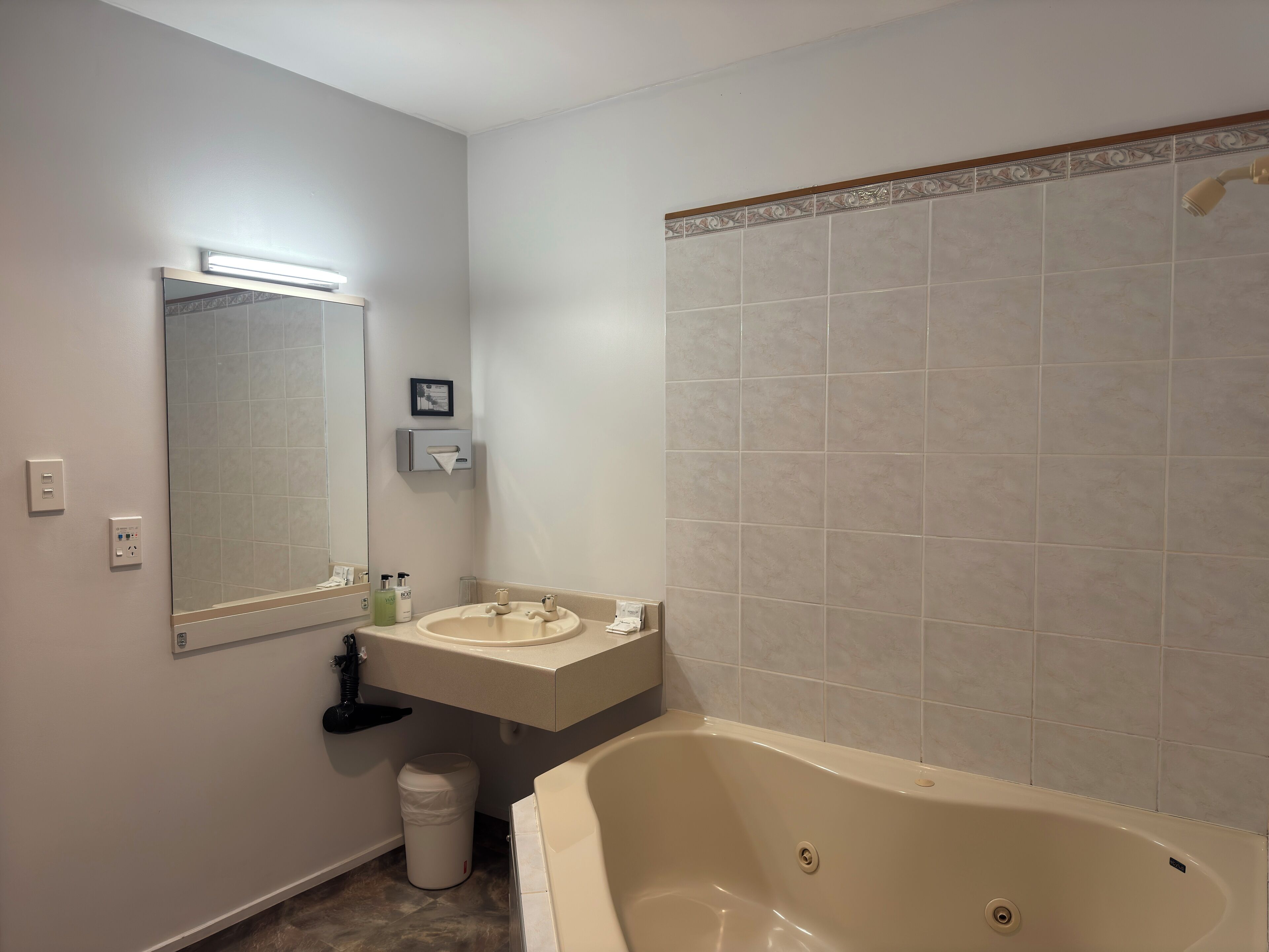 A bathroom with a bathtub, a sink, a mirror, and a trash bin.