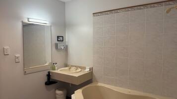 A bathroom with a bathtub, a sink, a mirror, and a trash bin.