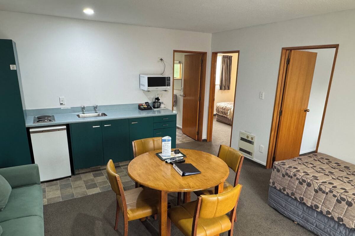 A compact living space with a kitchenette, a dining area with a round table and chairs, a single bed, and a small sofa.