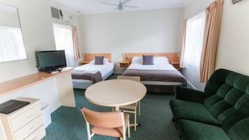 A hotel room with two single beds, a desk with a computer, a round table with two chairs, and a green sofa.