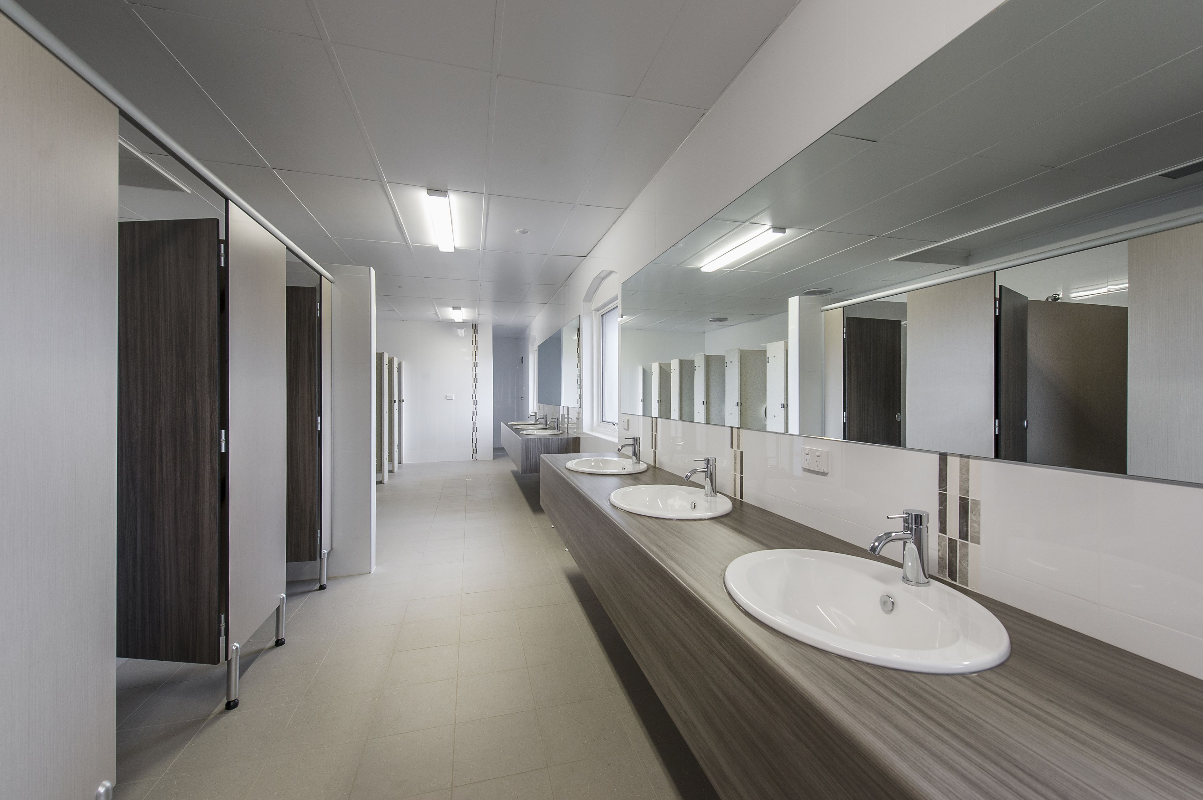 A modern restroom with long counters, multiple sinks, and mirrors.