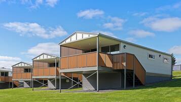 A modern multi-story building with a flat roof, wooden balcony railings, and a covered outdoor area.