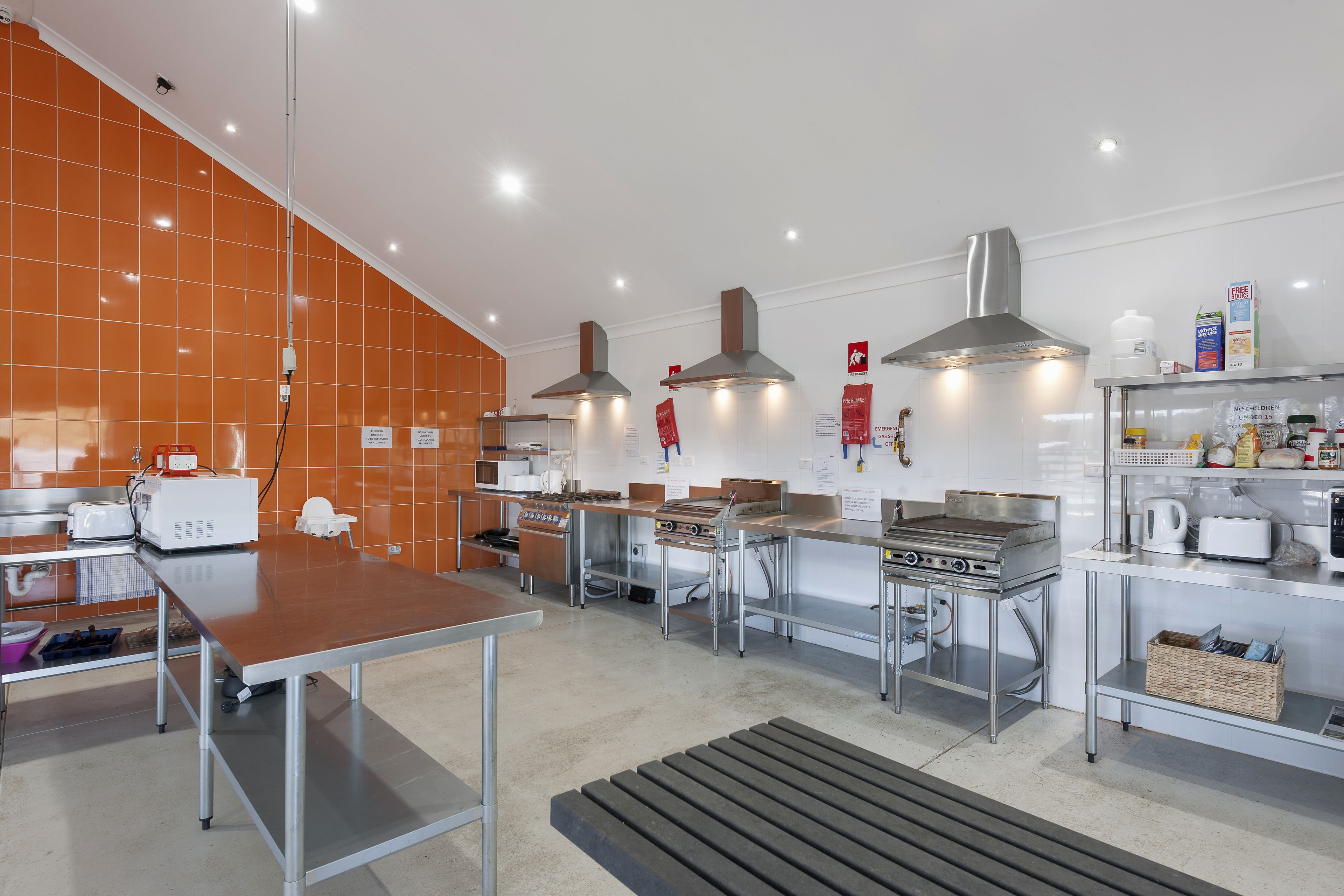 Une cuisine moderne dotée d’appareils électroménagers en acier inoxydable, d’une grande table et de murs recouverts de carreaux orange.