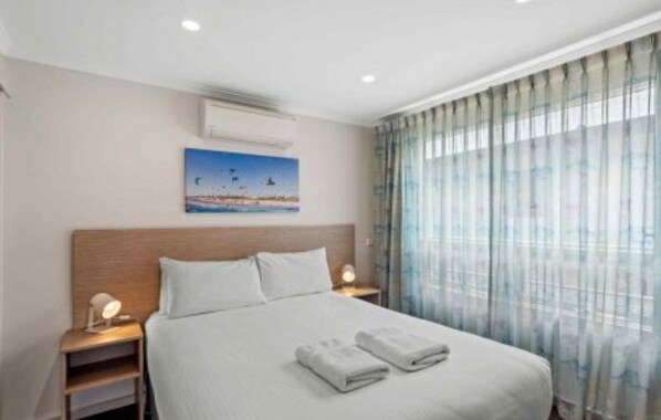 A hotel room with a large bed, two bedside tables with lamps, a painting on the wall, and a view through sheer curtains.