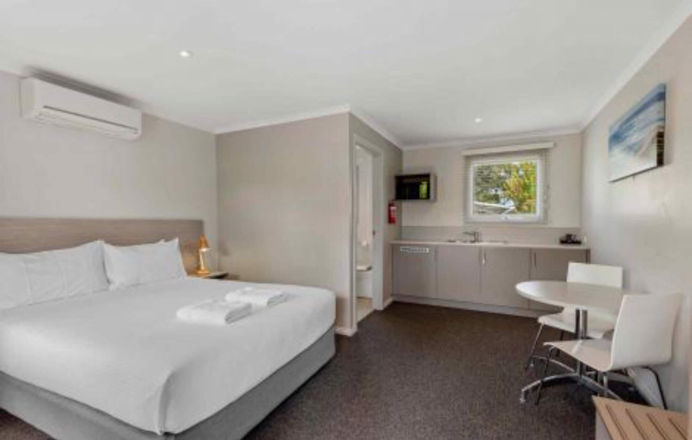 A hotel room with a bed, a small kitchenette, a dining table, and a TV.