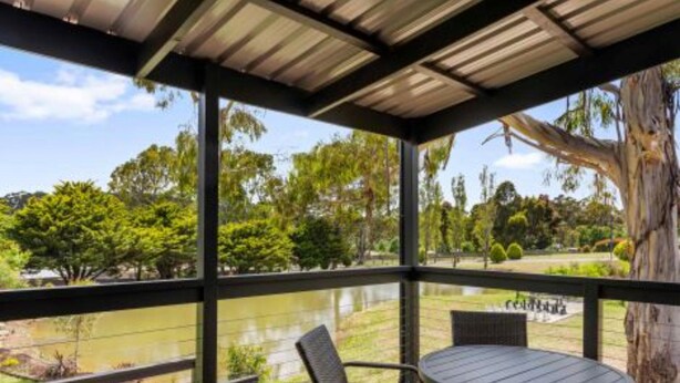 Un espacio de estar techado al aire libre con vista a un lago y árboles.