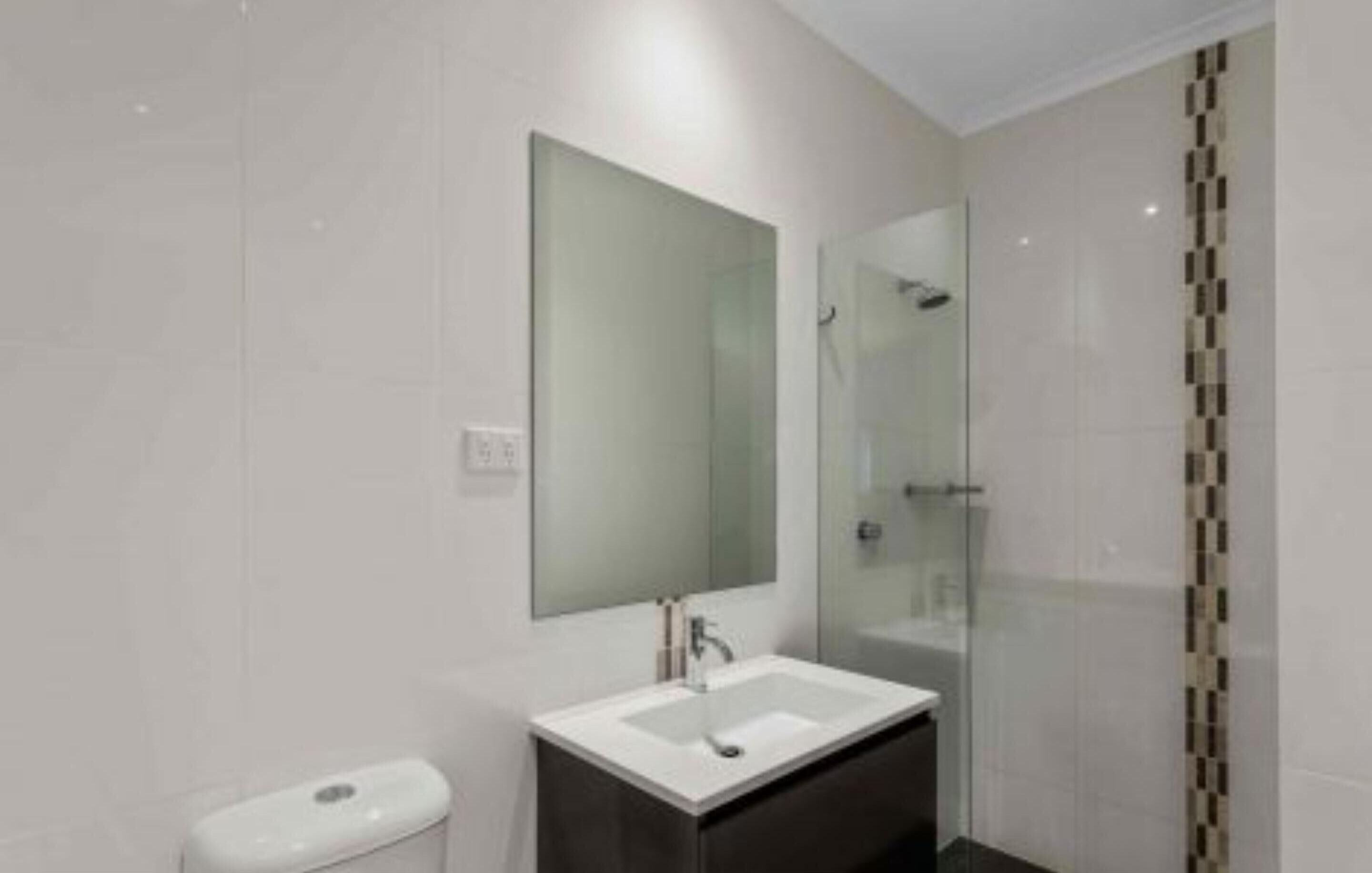Un baño moderno con cabina de ducha de vidrio, un lavabo blanco y un espejo grande.