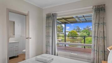 A bedroom with a bed, a bathroom with a toilet and sink, and a balcony with a view of greenery and a building.