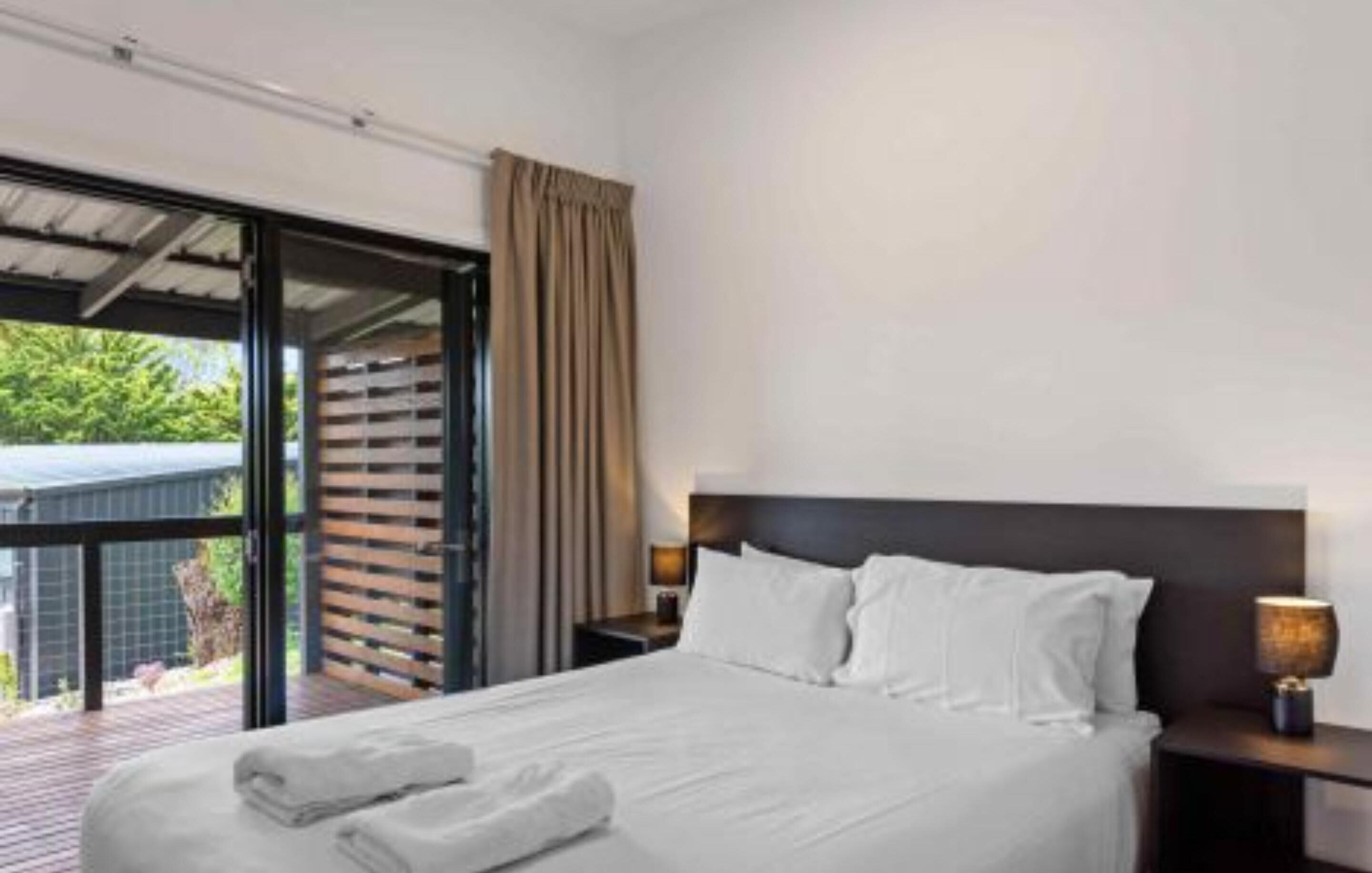 A modern hotel room with a large bed, a nightstand, and a window with a view of greenery.