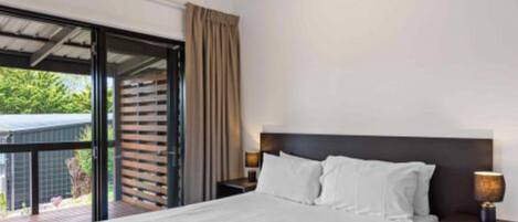 A modern hotel room with a large bed, a nightstand, and a window with a view of greenery.