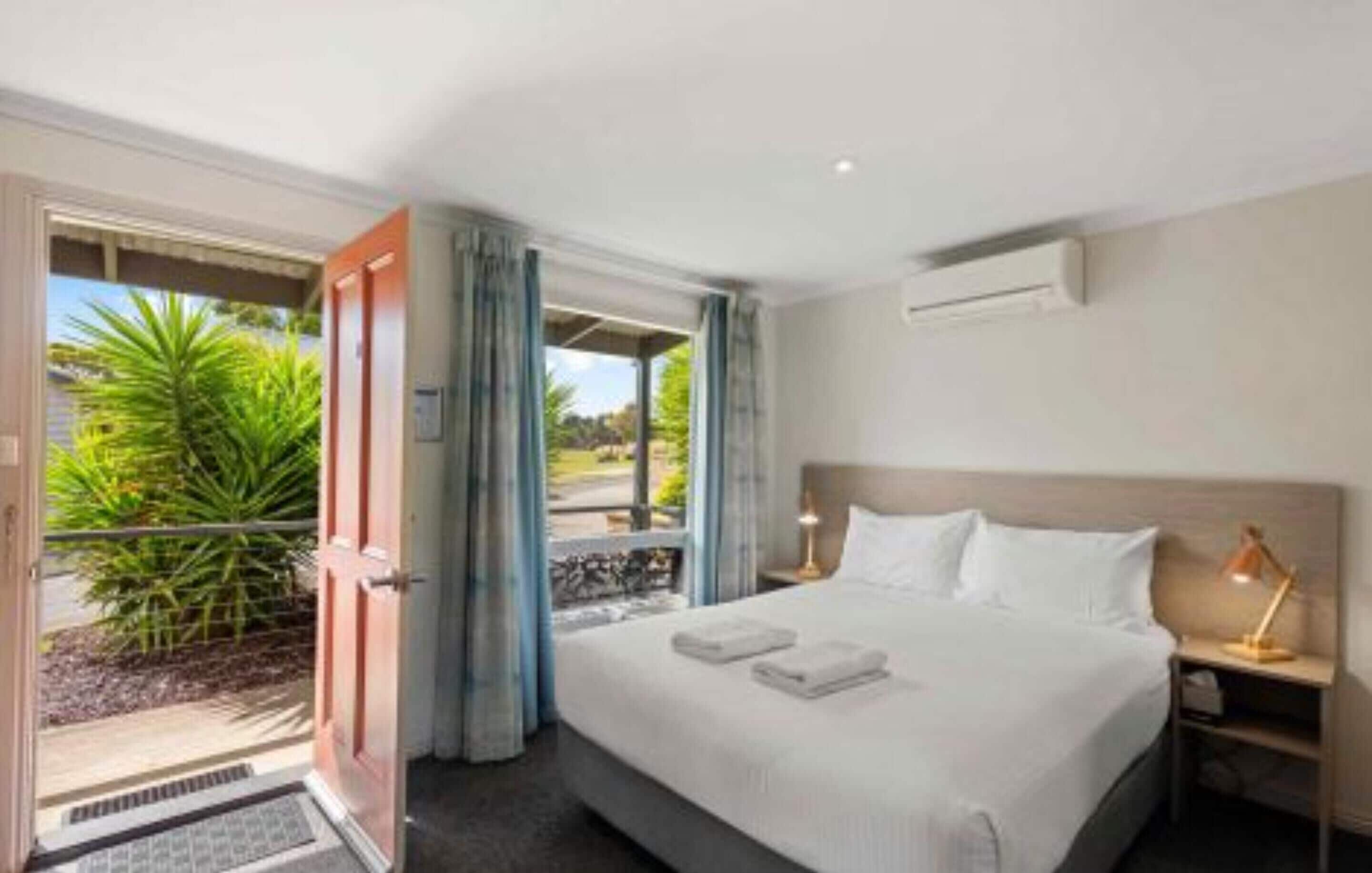 A hotel room with a bed, bedside lamps, a window with curtains, and a view of greenery outside.
