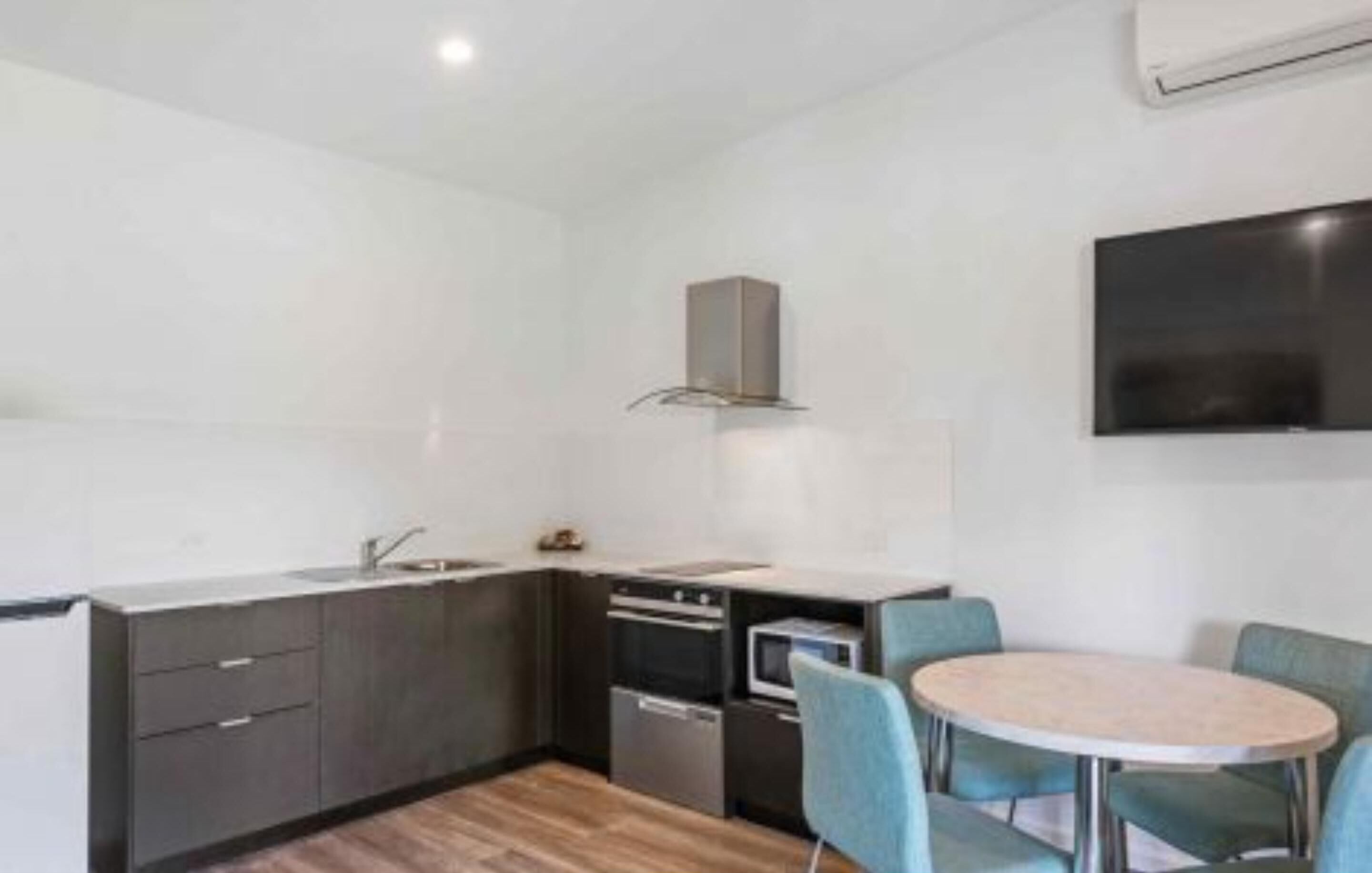 A compact kitchen with a built-in oven, a microwave, and a sink. There is a round table with four chairs.