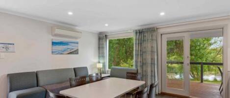 Una habitación moderna con una mesa grande, un sofá y un balcón con vistas a zonas verdes.