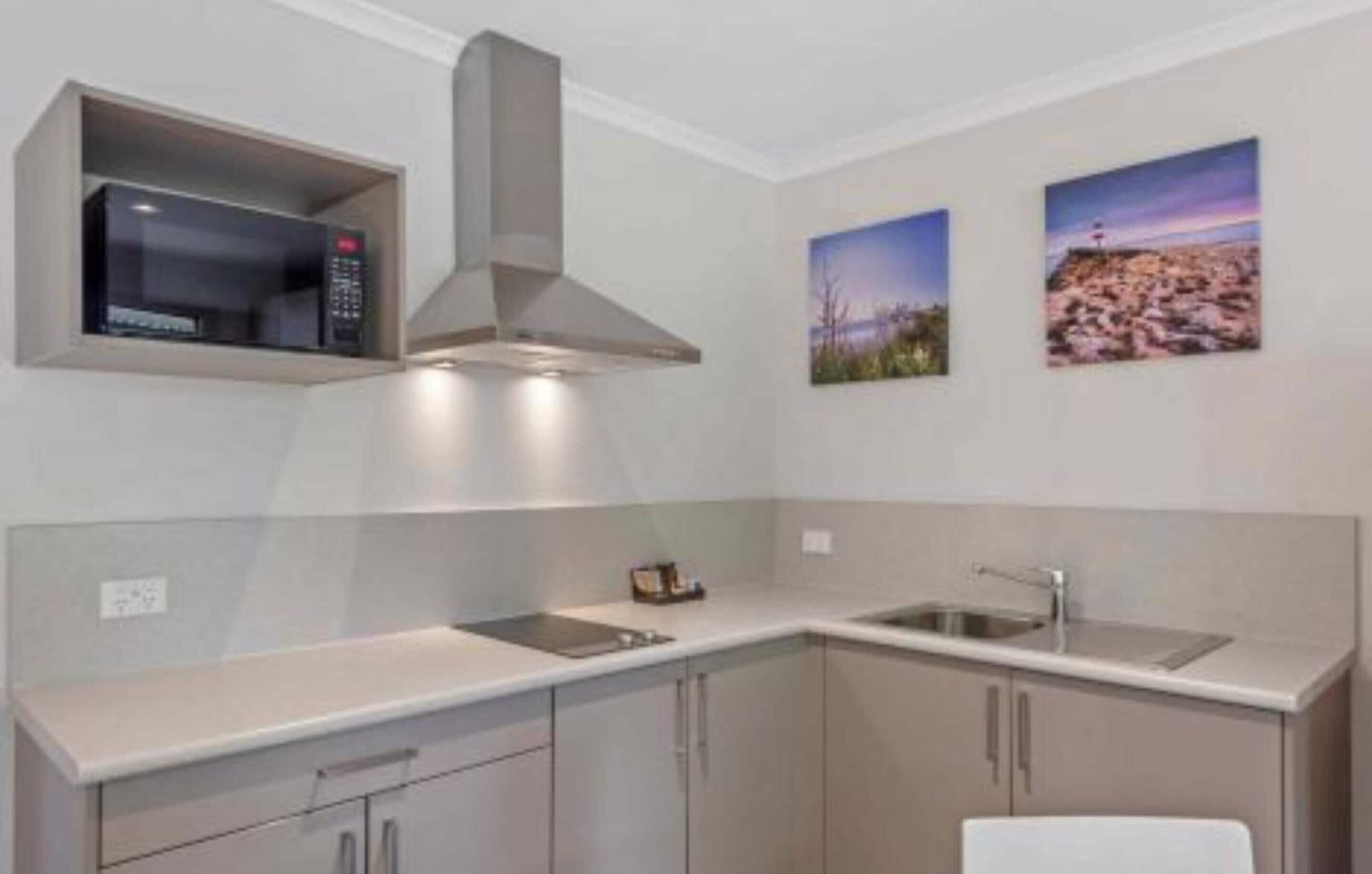 A modern kitchen with a microwave, double sink, and cabinets. There are two framed pictures on the wall.