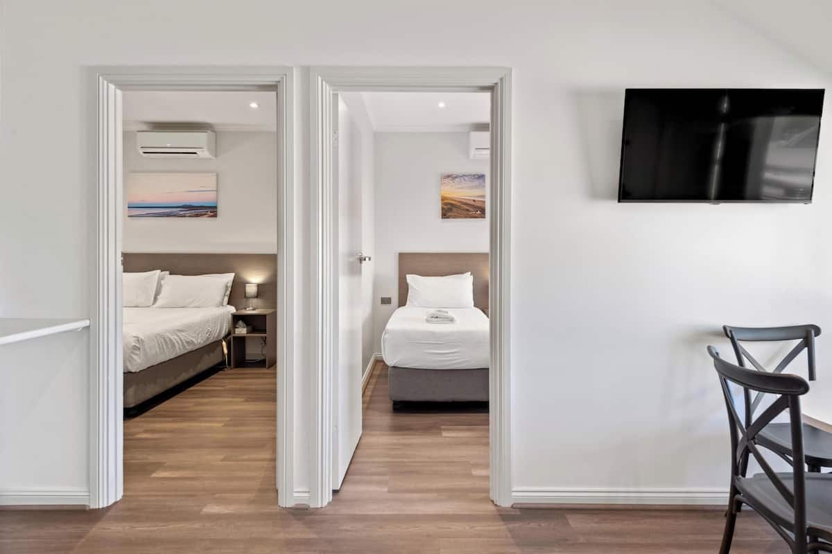 Hotellihuone, jossa on kaksi sänkyä, seinälle asennettu televisio ja puulattia.