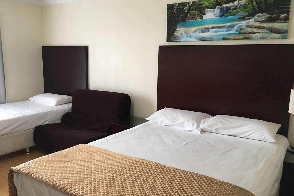 A hotel room with a large bed, a smaller bed, a chair, and a painting of a waterfall on the wall.