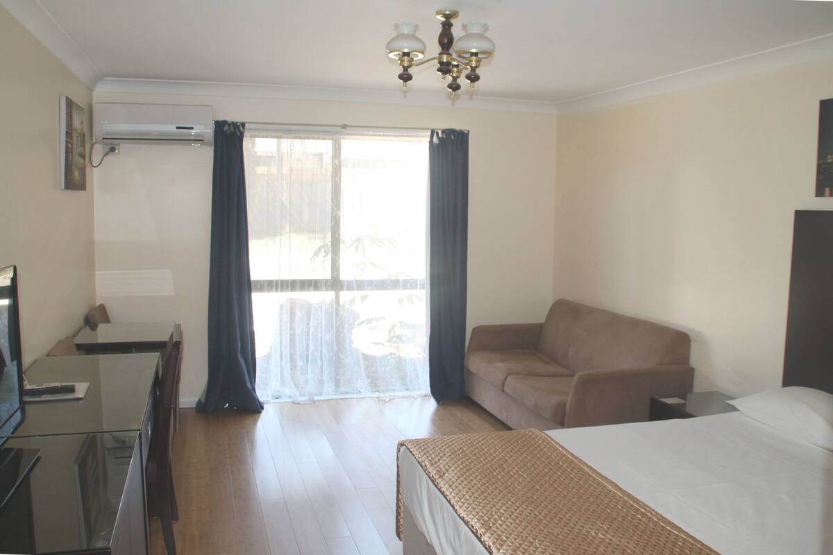 A hotel room with a bed, a sofa, a desk with a computer, and a window with curtains.
