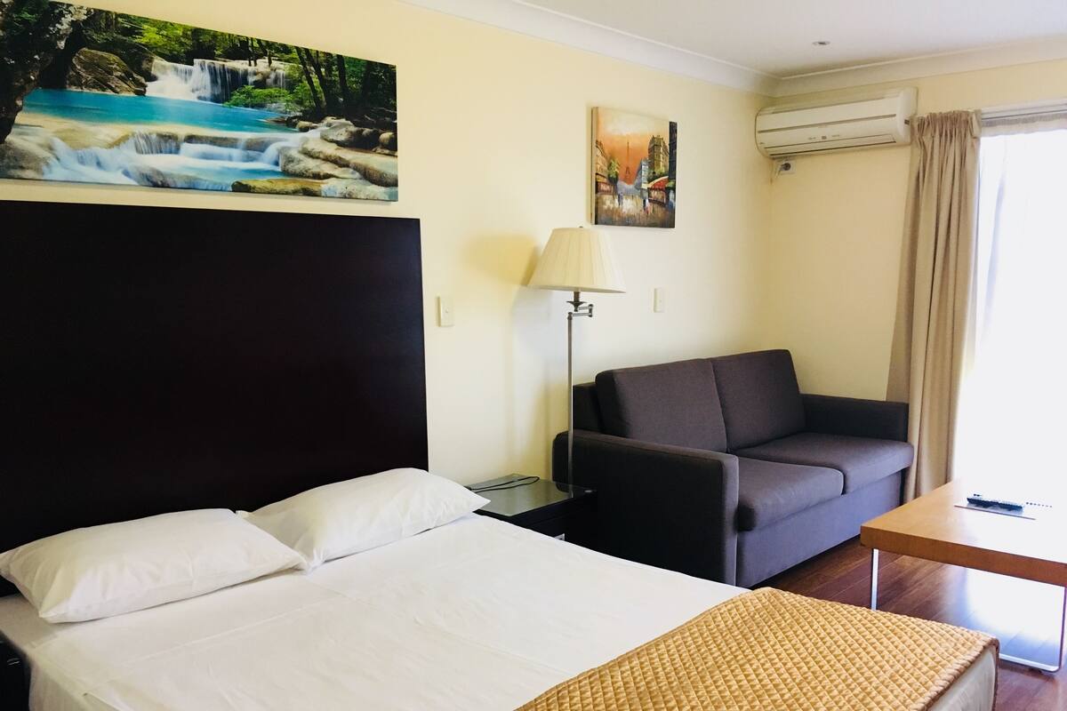 A hotel room with a bed, a sofa, a lamp, and artwork on the wall.